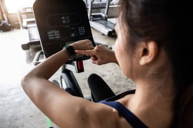 Genç kadın spor salonunda sağlıklı yaşam tarzında çalışıyor, kadın spor yaparken bisiklet ya da bisiklet sürerken akıllı saat kullanıyor.