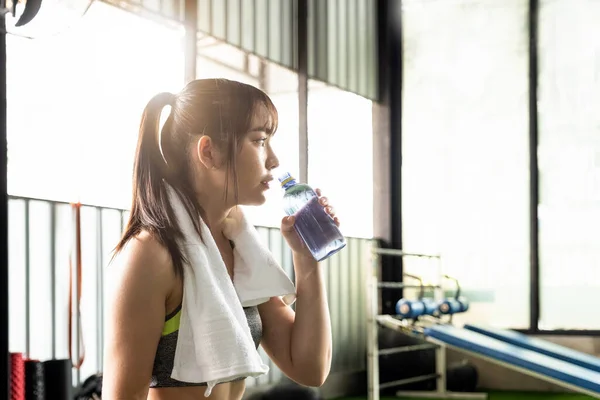 Молода азіатська спортсменка п'є воду після тренувань або фізичних вправ у фітнес-залі . — стокове фото