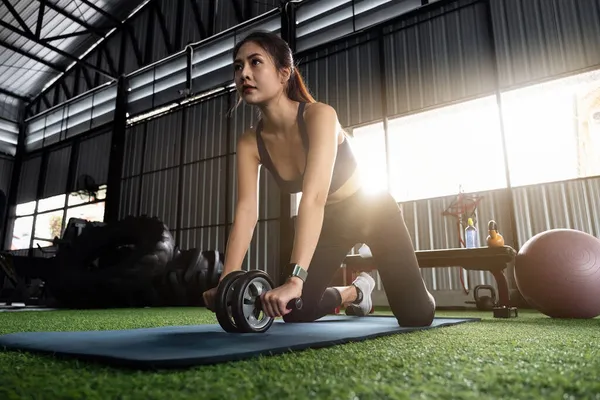 Κοντινό πλάνο της ασιατικής αθλητική γυναίκα κάνει ab roller άσκηση, ενώ εργάζονται έξω στο φόντο γυμναστήριο. Έννοια γυναίκα υγειονομική περίθαλψη. — Φωτογραφία Αρχείου