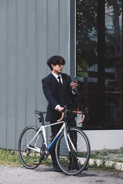 Portret azjatycki biznesmen pchanie jego rower rano z telefonu komórkowego — Zdjęcie stockowe