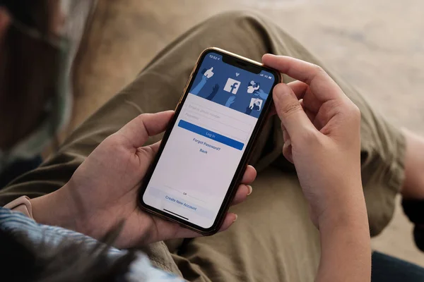 CHIANG MAI, THAILAND - NOV 7, 2021: Facebook közösségi média alkalmazás logó bejelentkezés, regisztráció az iPhone X mobilalkalmazás képernyőjén az e-kereskedelmi vásárlási üzletágon dolgozó személyek kezében. — Stock Fotó