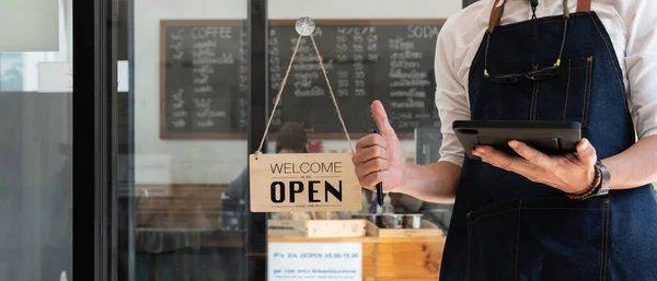Close up of Store owner turning open sign broad through the door glass and ready to serve. hotel service, cafe-restaurant, retail store, small business owner concept.