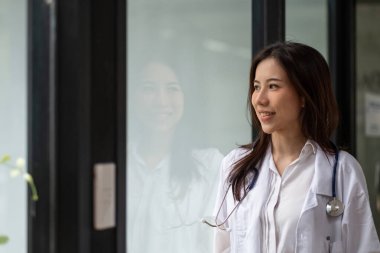 Hastaneden dışarı bakan mutlu Asyalı kadın doktor portresi.