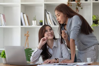 İki Asyalı iş arkadaşı birlikte çalışıyor. Ofiste dizüstü bilgisayar kullanıyorlar. Masasında da mali belgeler var.