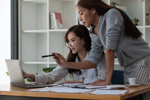 Deux collègues asiatiques travaillent ensemble, ont une répulsion, en utilisant un ordinateur portable au bureau avec un document financier sur le bureau — Photo
