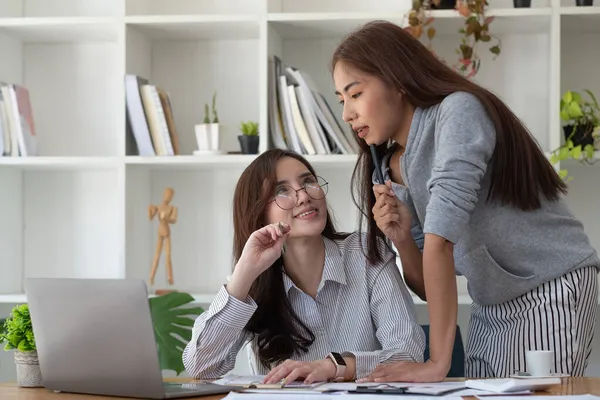 Twee Aziatische vrouwelijke collega 's die samenwerken, hebben een disussie, met behulp van laptop computer op kantoor met financieel document op het bureau — Stockfoto