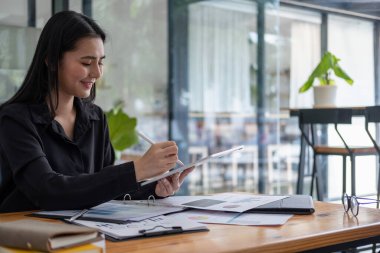 Evrak işleri ile uğraşırken dijital tablet kullanan çekici bir iş kadını.