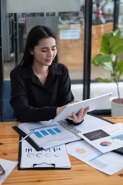 Empresária atraente usando um tablet digital enquanto trabalhava com papelada gráfico de dados financeiros em mesa de madeira. — Fotografia de Stock