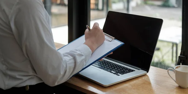 Mujer de negocios mano están tomando notas en papel con un bolígrafo, y ella está utilizando una computadora portátil en un escritorio de madera en la oficina.Banner web — Foto de Stock