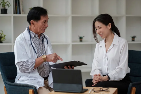 Leitender asiatischer Arzt berät junge Patientin, spricht mit Klientin beim Arztbesuch. Behandlung von geriatrischen Krankheiten. Altenpflegekonzept. — Stockfoto