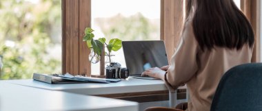 Back view of young asian businesswoman sitting on her workplace in the office. Young woman working for financial document data charts with laptop in the office.