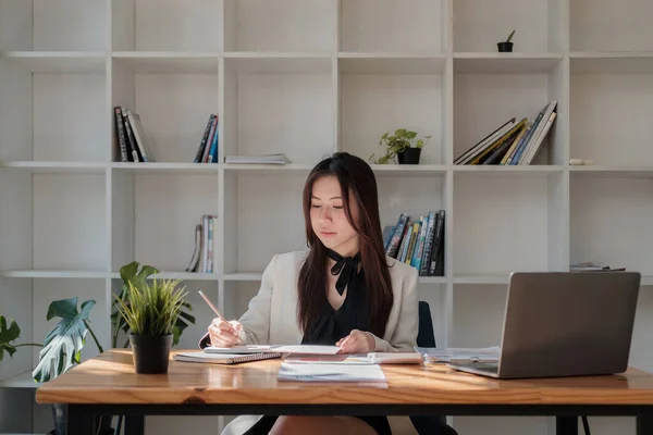 Ofisindeki not defterine not düşerken dizüstü bilgisayarla çalışan genç bir iş kadınının portresi. — Stok fotoğraf