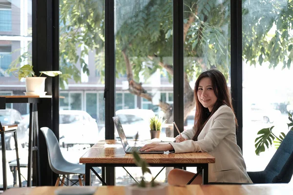 侧视年轻的亚洲女商人坐在办公室的工作场所。在办公室使用笔记本电脑为财务文件数据表工作的年轻妇女. — 图库照片