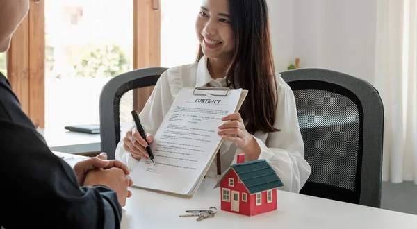 Fastighetsmäklare pekar på ett kontraktspapper och råder kunder att skriva under sina namn. teckna avtal om köp eller försäljning av hus. Koncept för fastighetskoncept — Stockfoto