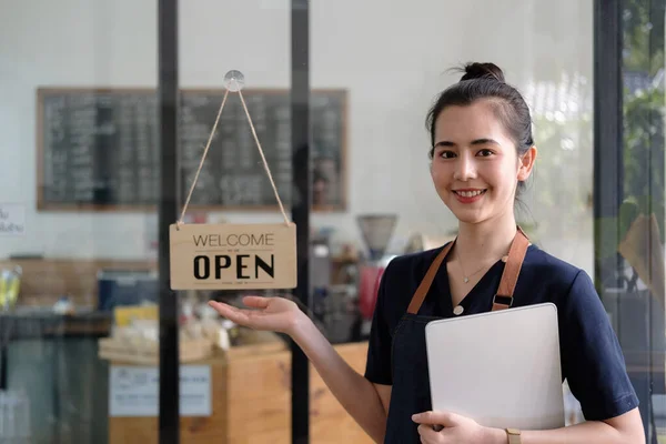 Linda asiática jovem barista mulher no avental segurando tablet e de pé na frente da porta do café com placa de sinal aberto. Iniciativa do empresário Conceito de empresário PME. — Fotografia de Stock