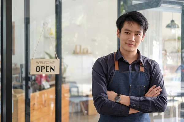 Inteligente asiático jovem barista macho no avental segurando tablet e de pé na frente da porta do café com placa de sinal aberto. Iniciativa do empresário Conceito de empresário PME — Fotografia de Stock