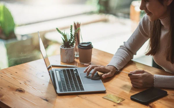 Genç Asyalı gülümseyen kadın evde dinleniyor ve alışveriş yapıyor. Bilgisayarı ve kredi kartını online alışveriş için kullanan mutlu kadın.