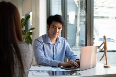 Genç Asyalı erkek portresi kameraya bakıyor ve dizüstü bilgisayar kullanıyor.