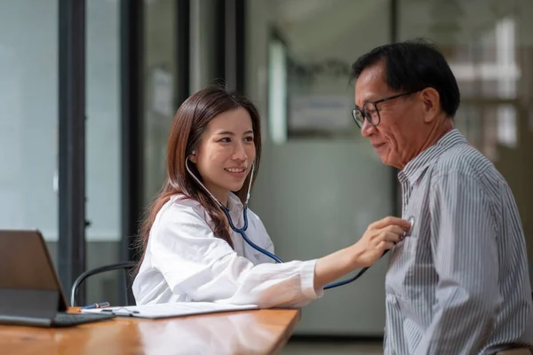 Stethoskopie-Untersuchung. Attraktive fröhliche asiatische Ärztin hört älteren Menschen zu, während sie Stethoskop benutzt — Stockfoto