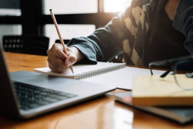 Asyalı bir kadının not defterine not tutarken ya da içeriden bilgisayar öğrenirken çekilmiş fotoğrafı. Eğitim kursu, seminer, eğitim, çevrimiçi eğitim kavramı.