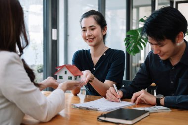 Emlakçı, ev almak ya da satmak için müşteri sözleşmesi imzası için el uzatıyor. Mutlu Asyalı çift ofiste bir kontrat imzalıyor. Gayrimenkul sözleşmesi kavramı