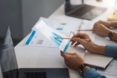 İş adamları, kavramsal iş danışmanlığı ofisinde veri, grafik ve mali raporları analiz eder, tartışır ve beyin fırtınası yapar. Masada hesap makinesi kullanan bir muhasebeci.