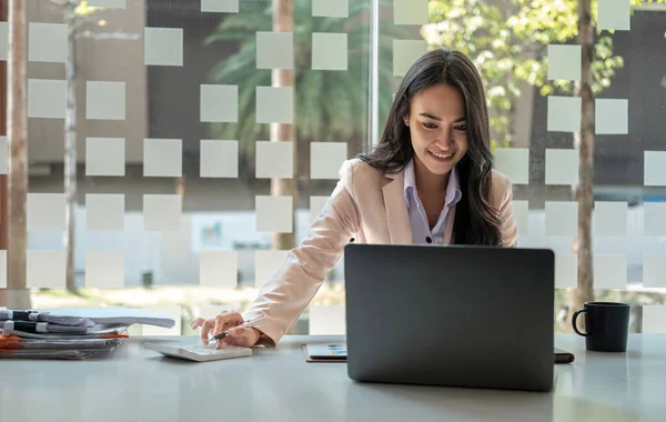 Atractiva mujer de negocios asiática sentada trabajando en computadora portátil y calculadora con documentos financieros en la oficina — Foto de Stock