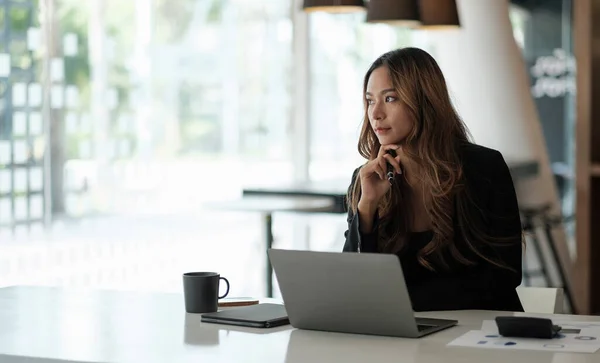 Πορτρέτο της ασιάτισσας επιχειρηματία που κάθεται με φορητό υπολογιστή κοιτάζοντας έξω, ενώ εργάζονται με γραφειοκρατία στο γραφείο — Φωτογραφία Αρχείου