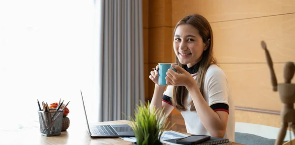 Портрет улыбающейся красивой азиатской женщины, расслабляющей, используя технологию ноутбука, сидя на столе. — стоковое фото