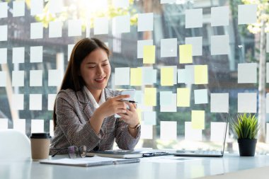 İş kadını mali raporları hesaplamak için cep telefonu ve laprop bilgisayar kullanıyor ve danışmanlık için bankacıyı arıyor.