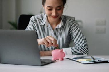 Asyalı kadın para biriktirmek ve finansal konsept için domuzcuğa para yatırıyor..