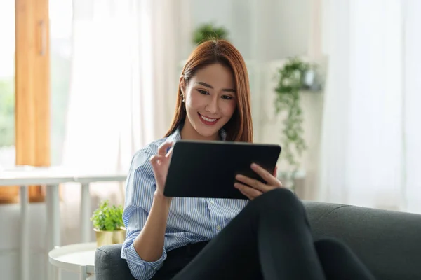 Очаровательная азиатская женщина, использующая цифровой планшет для онлайн-шопинга чата на диване в гостиной. — стоковое фото