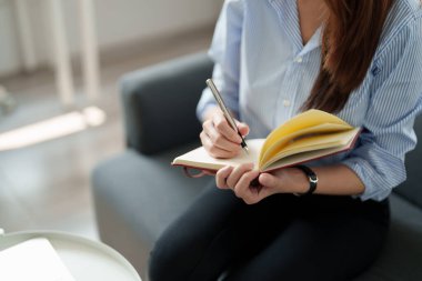 Bir kadının not defterine not alırken çekilmiş fotoğrafı. Kapalı alanda çalışırken ya da öğrenirken. Eğitim kursu, seminer, eğitim, çevrimiçi eğitim konsepti.