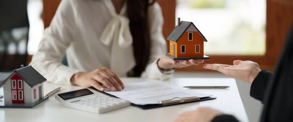 Immobilienmakler stimmen zu, ein Haus zu kaufen und Kunden in ihren Agenturen ein kleines Hausmodell zu geben. — Stockfoto
