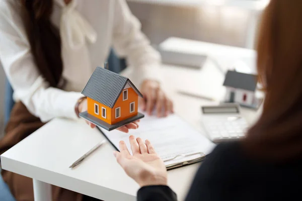 Immobilienmakler stimmen zu, ein Haus zu verkaufen und Kunden in ihren Agenturen ein Modell für ein kleines Haus zu geben. — Stockfoto