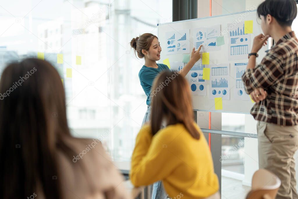 group of young creative asian people doing brainstorming meeting colleagues in board room discussing project. woman standing at white board give presentation
