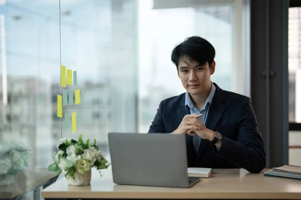 Joven asiático hombre de negocios sonriendo mientras trabaja con ordenador portátil en la oficina, concepto de oficina de negocios —  Fotos de Stock