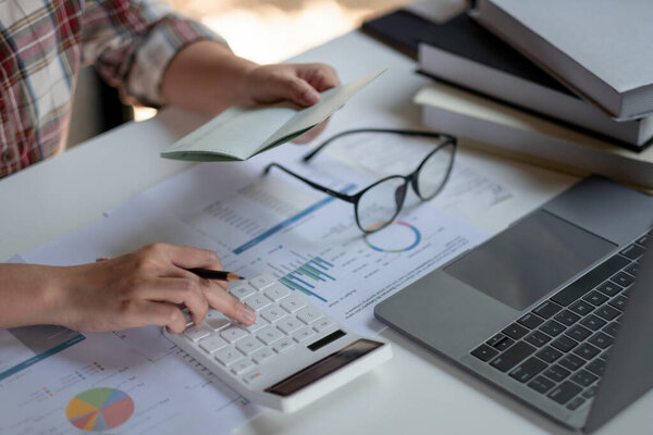 woman checking amount in bank account passbook with bank statement. Accountant using calculator for financial