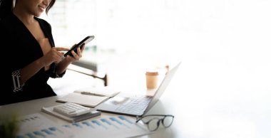 Akıllı telefon tutan Asyalı bir kadın iş için hesap makinesi kullanırken finansal hesaplama para banka kredi kira ödemeleri harcamalar finansman vergiler evrak konsepti, kapatma.