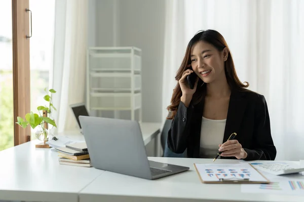 Asyalı İş Kadını Cep Telefonuyla Konuşuyor Modern Ofiste finansal işler için dizüstü bilgisayarla çalışıyor. — Stok fotoğraf