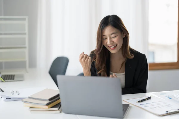 행복 한 젊은 아시아인 사업가가 온라인에서 좋은 소식에 흥분 한 노트북을 보고 있습니다. 운좋게 도 성공 한 남자 가 사무실 책상에 앉아 — 스톡 사진