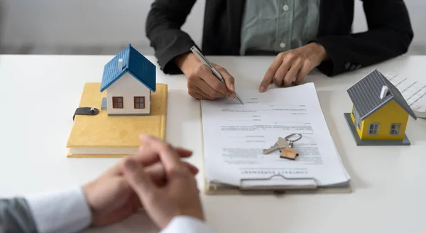 Agente imobiliário auxiliando cliente a assinar contrato em mesa com modelo de casa — Fotografia de Stock