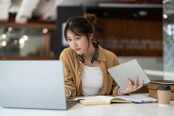 Sorrindo asiática jovem do sexo feminino usando fone de ouvido olhando para tela do laptop ouvir e aprender cursos on-line. Mulher de negócios feliz com fones de ouvido chamada de vídeo para atendimento ao cliente — Fotografia de Stock