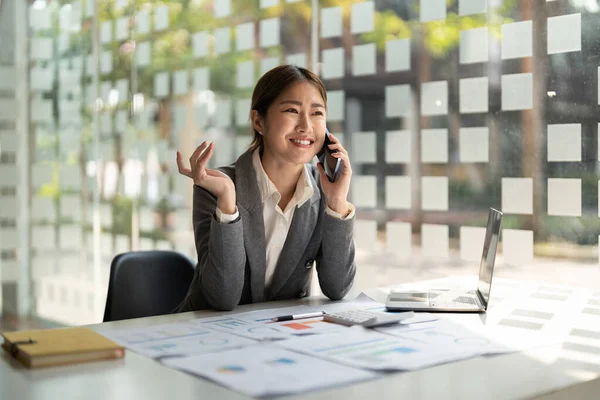 Sonriente negocio asiático mujer en hablando consultor en móvil en moderno oficina — Foto de Stock