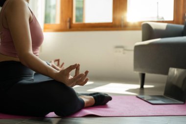 Asyalı kadın diz üstü bilgisayarla antrenörle meditasyon yapıyor. Nilüfer pozisyonunda yoga minderinin üzerinde oturan sağlıklı kadın.