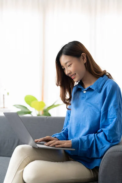 Junge asiatische Geschäftsfrau lächelt und arbeitet von zu Hause mit Laptop-Computer online zum Internet auf Sofa im Wohnzimmer, freiberufliche Mädchen mit Notizbuch auf Couch mit Komfort, neue normale, Lifestyle-Konzept — Stockfoto