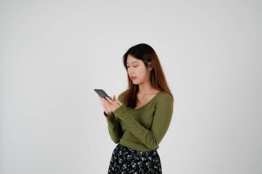 Genç Asyalı kadının portresi cep telefonundan arıyor, Asyalı kadının çekiciliği akıllı telefonuyla konuşuyor ve beyaz arka planda iletişim kurarken gülümsüyor..
