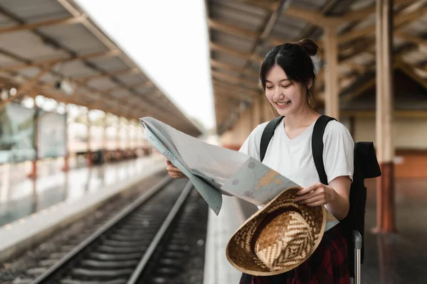 年轻的女旅行家背着背包，在火车站火车站的火车站站台上，一边等火车一边看地图。假日、旅行、旅行和夏季旅行概念 — 图库照片