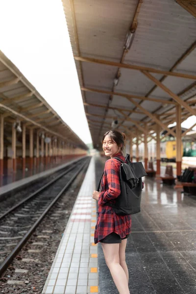 Portrait young Asian woman backpacker traveler walking alone at train station platform with backpack. Asian woman waiting train at train station for travel. Summer holiday traveling concept. — ストック写真