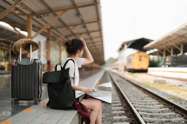 Viajero joven con mochila mirando al mapa mientras espera el tren, mochilero asiático en la plataforma ferroviaria en la estación de tren. Vacaciones, viaje, viaje y verano concepto de viaje de verano — Foto de Stock